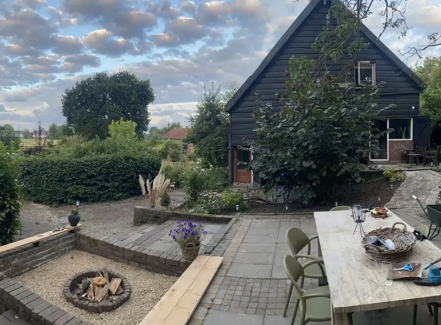 De BnB van ADAM: een donker houten huis met tuin, vuurplek en een grote tafel