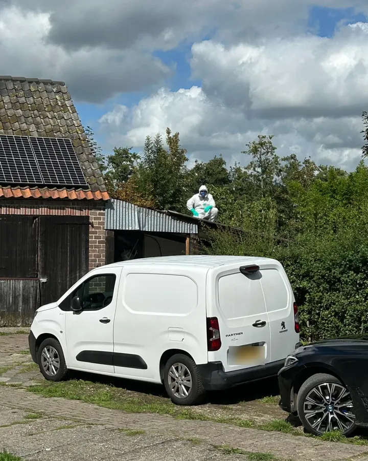 Medewerker in wit werkpak en met ademmasker op het dak van een schuur